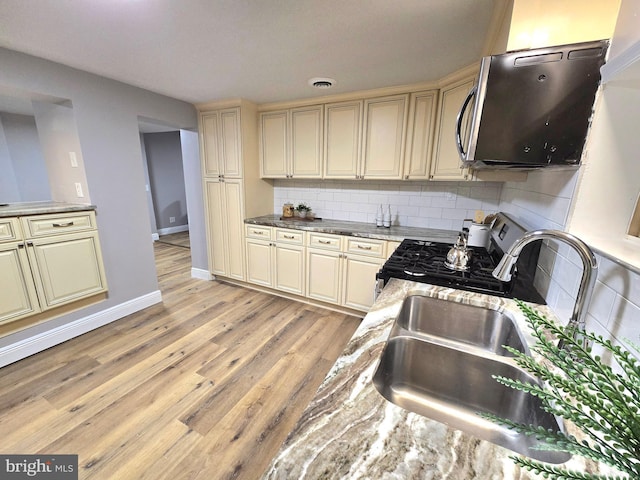 kitchen featuring decorative backsplash, cream cabinets, gas stove, and sink