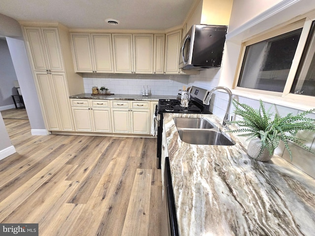 kitchen featuring appliances with stainless steel finishes, tasteful backsplash, sink, light hardwood / wood-style flooring, and cream cabinetry