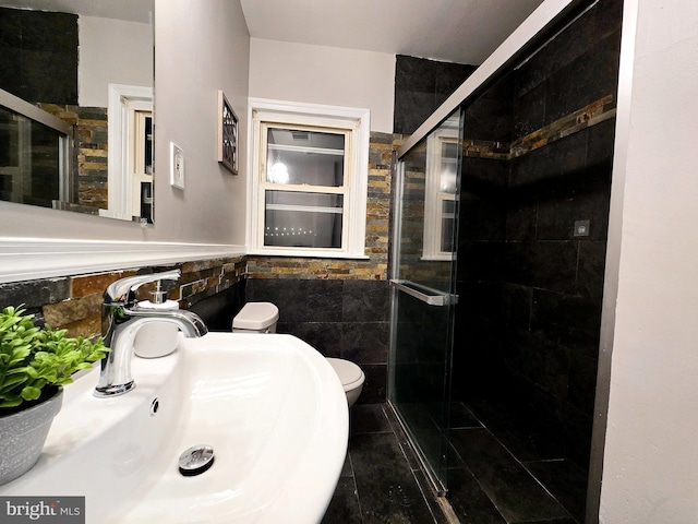 bathroom featuring sink, a shower with shower door, tile walls, and toilet