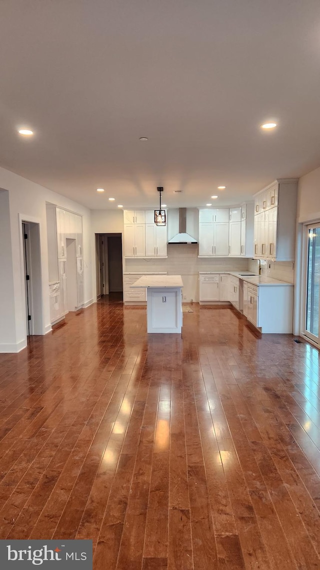 kitchen featuring hanging light fixtures, wall chimney range hood, a kitchen island, dark hardwood / wood-style floors, and white cabinets