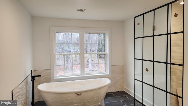 bathroom with tile patterned floors, plenty of natural light, a bathing tub, and tile walls