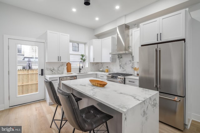 kitchen with high end appliances, a kitchen breakfast bar, wall chimney range hood, a wealth of natural light, and a kitchen island