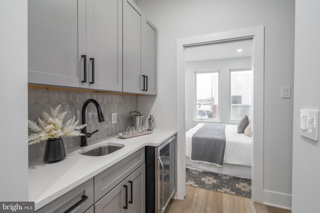 bar featuring wine cooler, light hardwood / wood-style flooring, gray cabinetry, and sink