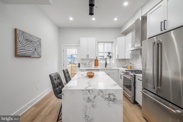 kitchen featuring white cabinetry, a center island, wall chimney range hood, high quality appliances, and a breakfast bar