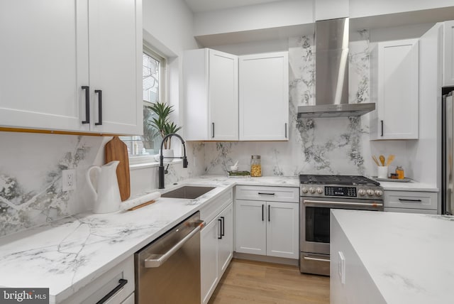 kitchen featuring white cabinetry, sink, stainless steel appliances, wall chimney range hood, and light hardwood / wood-style floors