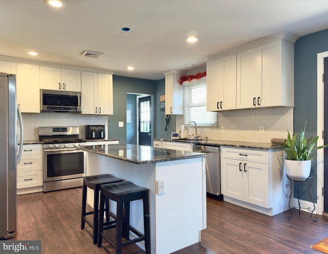 kitchen featuring dark wood-type flooring, appliances with stainless steel finishes, a kitchen island, white cabinetry, and a breakfast bar area