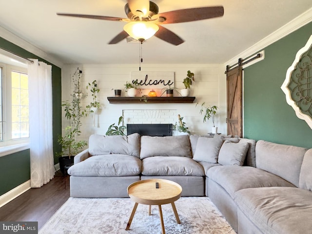 living room featuring ceiling fan, a brick fireplace, a barn door, dark hardwood / wood-style flooring, and ornamental molding