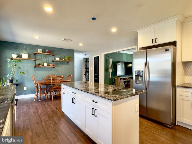 kitchen with dark wood-type flooring, dark stone counters, white cabinets, stainless steel fridge, and a kitchen island