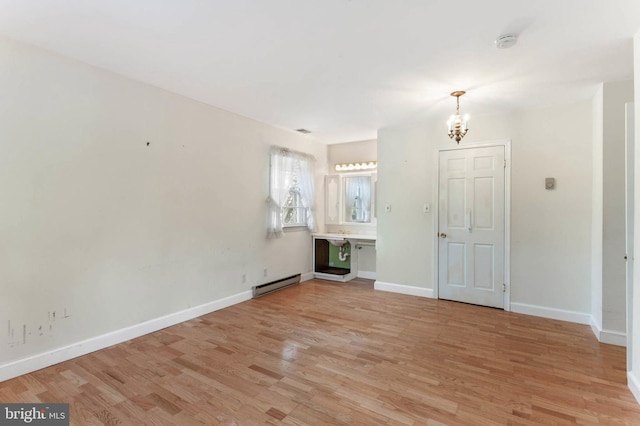 unfurnished living room featuring a baseboard radiator, light hardwood / wood-style floors, and a notable chandelier