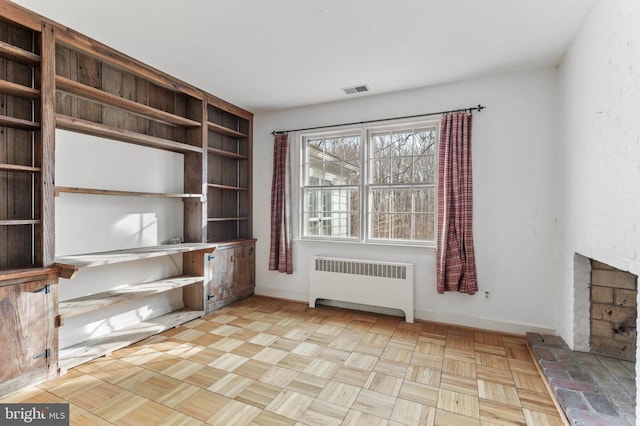 unfurnished office featuring radiator heating unit, light parquet floors, and a brick fireplace