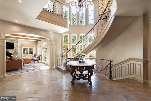 entrance foyer with a stone fireplace, a high ceiling, decorative columns, and a notable chandelier