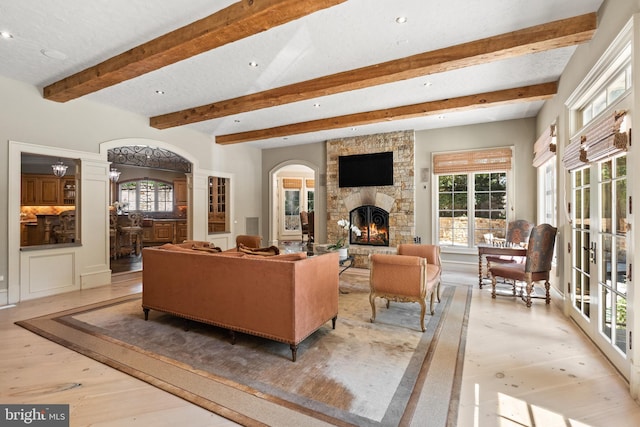 living room featuring beam ceiling, a stone fireplace, a textured ceiling, and light wood-type flooring