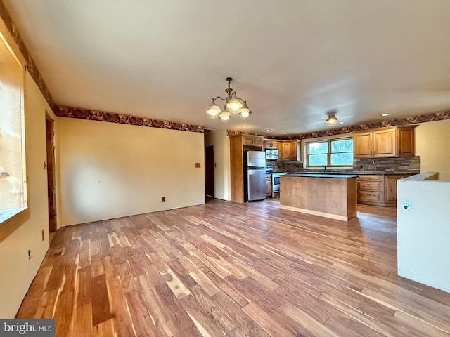 kitchen with a center island, stainless steel appliances, light hardwood / wood-style flooring, backsplash, and a chandelier