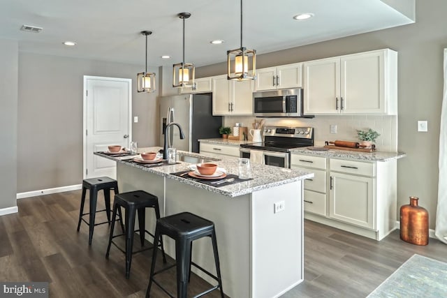 kitchen with light stone countertops, dark hardwood / wood-style flooring, stainless steel appliances, and an island with sink