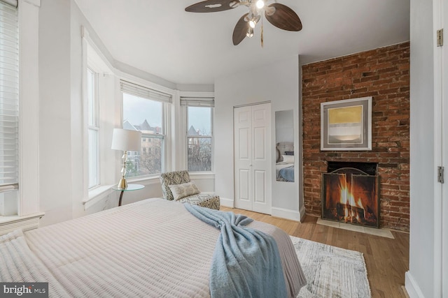 bedroom featuring baseboards, a ceiling fan, wood finished floors, a fireplace, and a closet