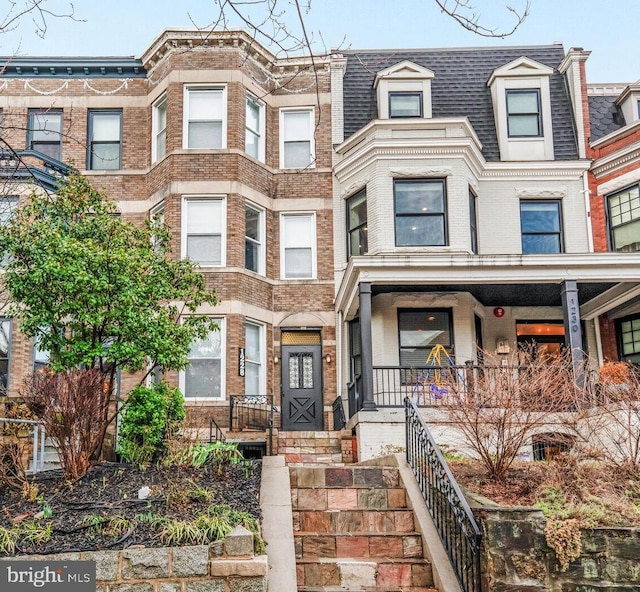 townhome / multi-family property featuring mansard roof, brick siding, roof with shingles, and covered porch