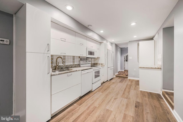 kitchen with white appliances, a sink, white cabinetry, light wood-style floors, and tasteful backsplash