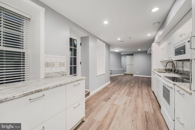 kitchen with white appliances, light wood finished floors, decorative backsplash, white cabinetry, and a sink