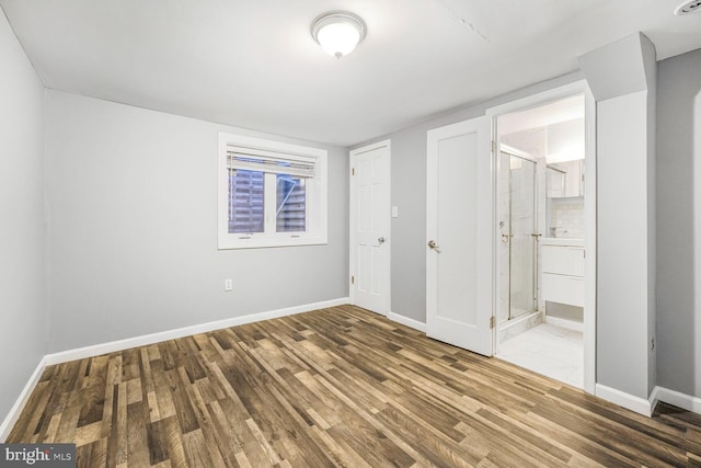 unfurnished bedroom featuring wood finished floors, connected bathroom, and baseboards