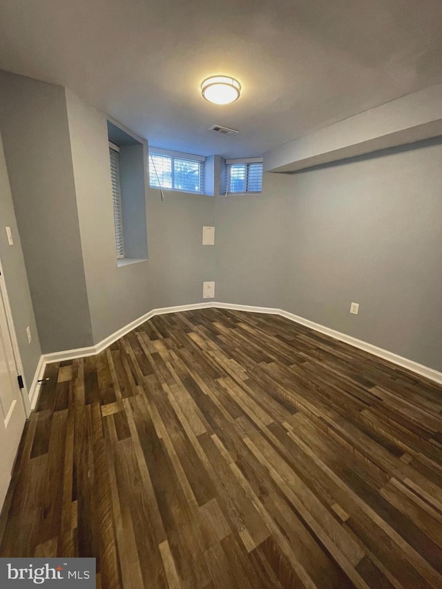 basement featuring dark wood-type flooring, visible vents, and baseboards