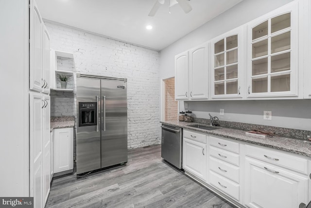 kitchen featuring stainless steel appliances, a sink, white cabinetry, light wood finished floors, and glass insert cabinets