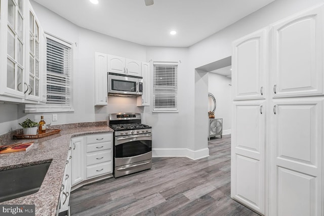 kitchen featuring stainless steel appliances, wood finished floors, glass insert cabinets, and white cabinets