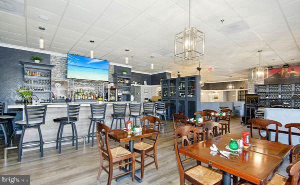 dining area featuring a paneled ceiling, wood finished floors, and a community bar