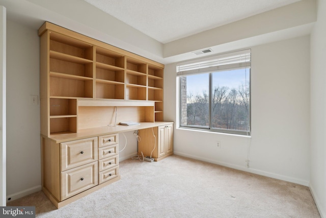 unfurnished office with light colored carpet, visible vents, built in study area, a textured ceiling, and baseboards