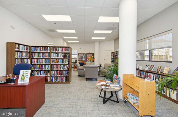 sitting room featuring wall of books and a drop ceiling