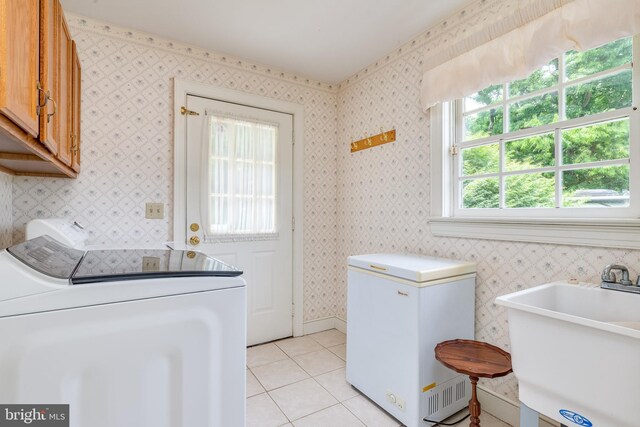 clothes washing area with washing machine and clothes dryer, light tile patterned floors, cabinets, and sink