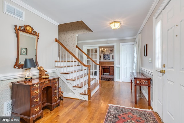 foyer featuring crown molding, hardwood / wood-style floors, an inviting chandelier, and a brick fireplace