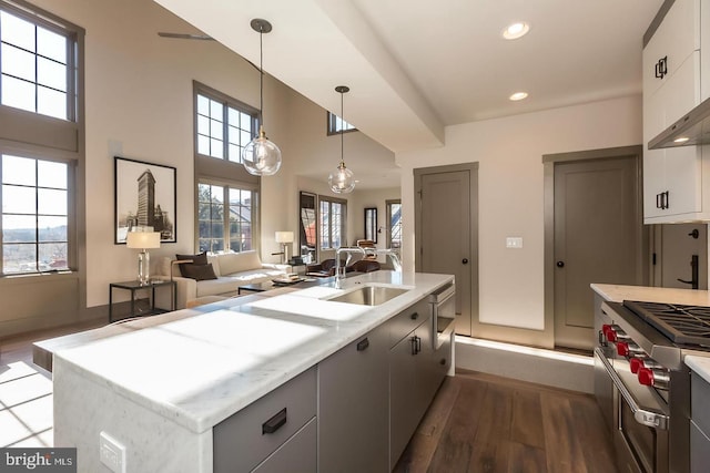 kitchen with white cabinetry, sink, dark wood-type flooring, decorative light fixtures, and a center island with sink