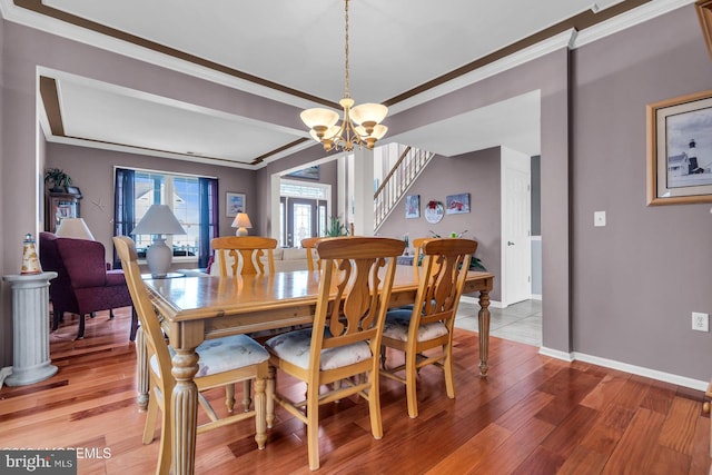 dining space with wood-type flooring, ornamental molding, and a chandelier