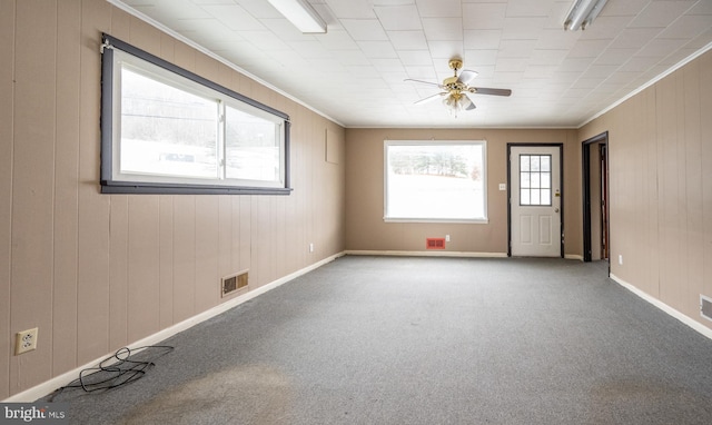 unfurnished room with carpet floors, ceiling fan, crown molding, and wood walls