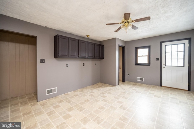 laundry area with ceiling fan, cabinets, and a textured ceiling