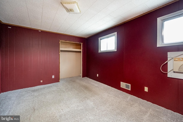 unfurnished bedroom featuring carpet floors, ornamental molding, wooden walls, and a closet