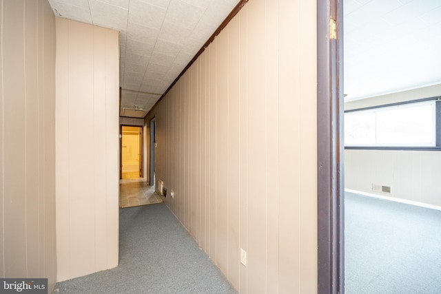 corridor with light carpet, crown molding, and wood walls