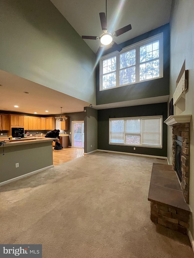 unfurnished living room with a fireplace, a towering ceiling, light colored carpet, and ceiling fan with notable chandelier