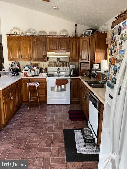 kitchen with a textured ceiling, lofted ceiling, sink, and white appliances