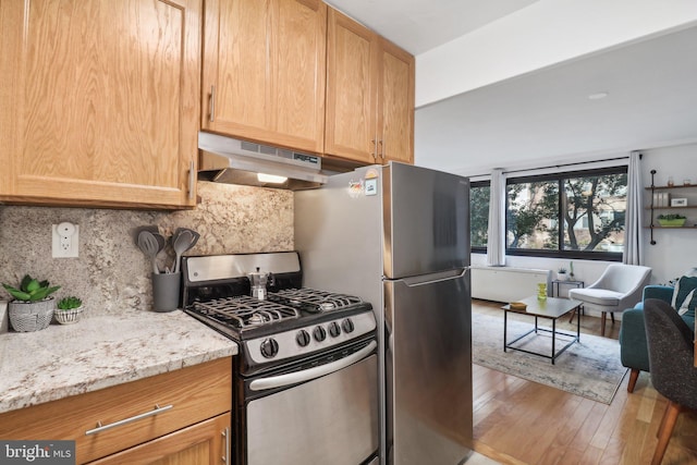 kitchen featuring stainless steel appliances, light stone counters, backsplash, light hardwood / wood-style floors, and exhaust hood