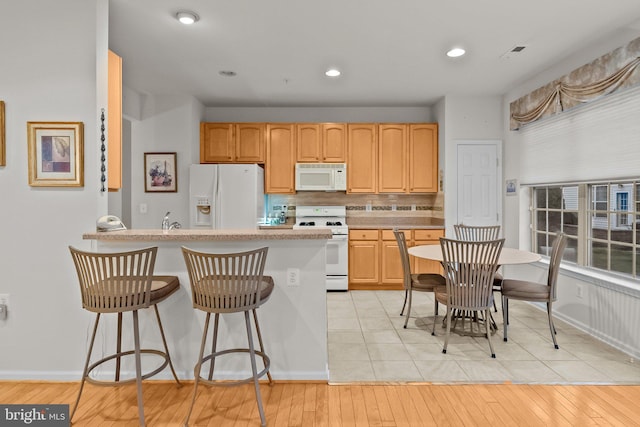 kitchen with a kitchen breakfast bar, light brown cabinets, light hardwood / wood-style floors, and white appliances