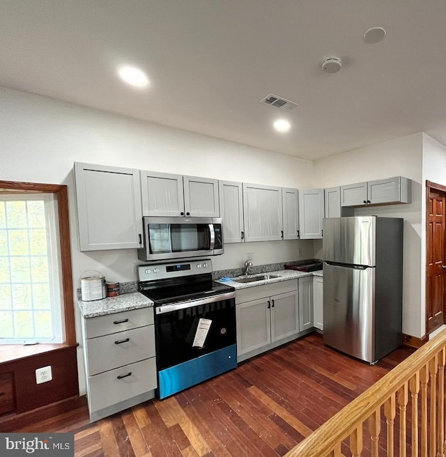 kitchen with dark wood-type flooring, sink, gray cabinets, light stone counters, and stainless steel appliances