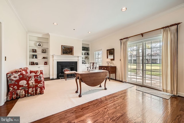 living room with built in features, hardwood / wood-style flooring, a brick fireplace, and crown molding