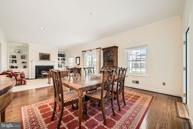 dining room with hardwood / wood-style floors, built in shelves, and crown molding