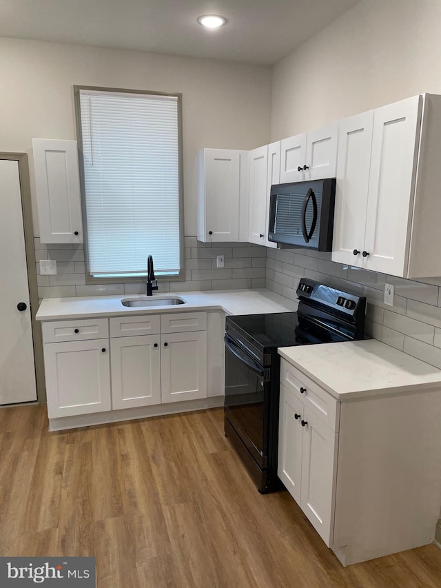 kitchen featuring black range with electric stovetop, white cabinetry, sink, and light hardwood / wood-style floors