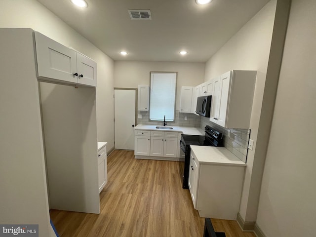 kitchen with decorative backsplash, light wood-type flooring, sink, black appliances, and white cabinetry