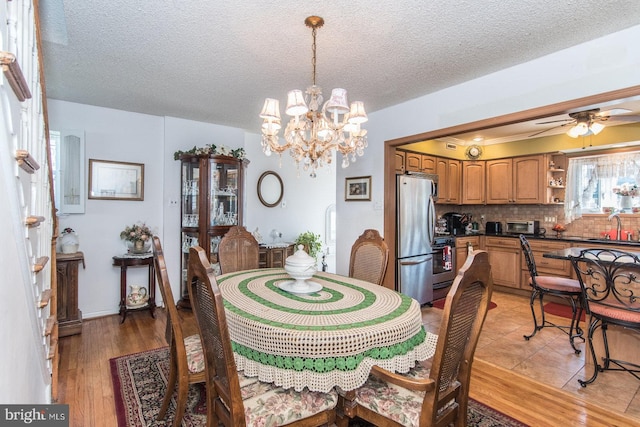 dining space with a textured ceiling, ceiling fan with notable chandelier, light hardwood / wood-style floors, and sink