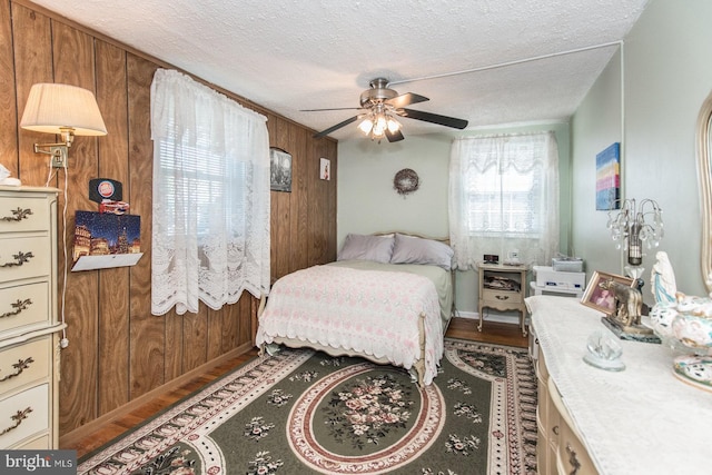 bedroom featuring a textured ceiling, hardwood / wood-style flooring, ceiling fan, and wood walls