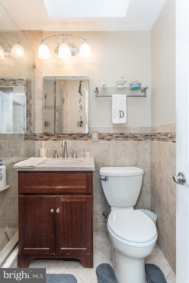 bathroom with toilet, vanity, tile patterned floors, and tile walls