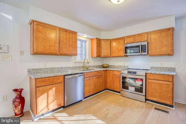 kitchen with light stone countertops, stainless steel appliances, light hardwood / wood-style floors, and sink